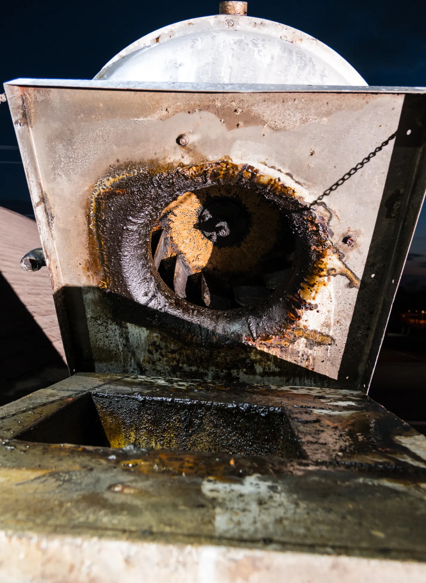 about-1 A metal vent hood with extensive fire damage and soot, showing a large burned hole and charred residue inside.