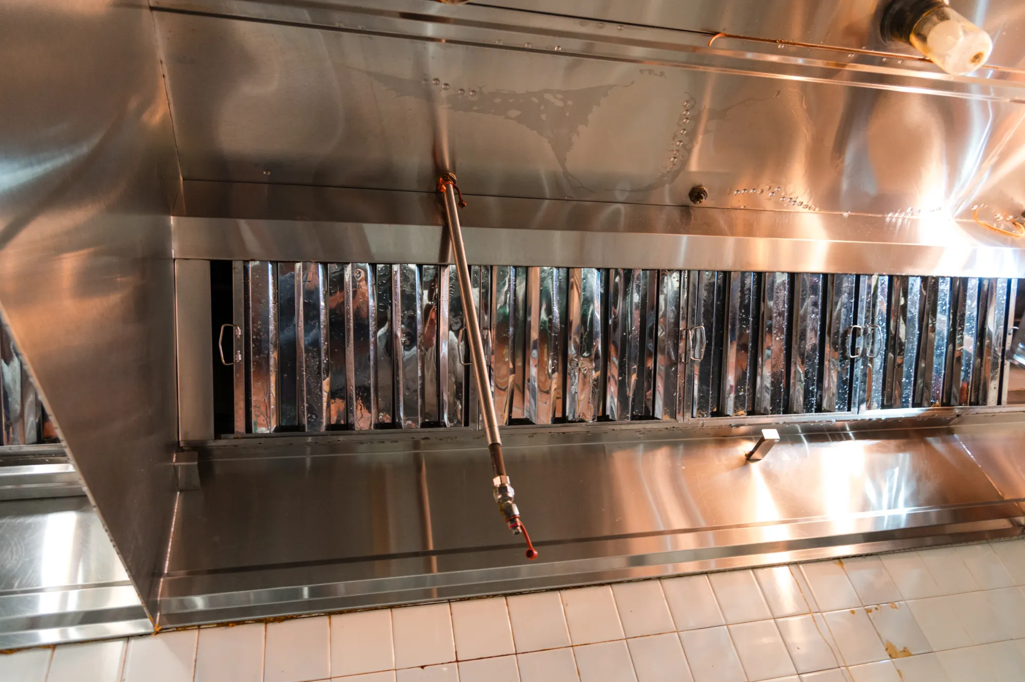 A commercial kitchen's stainless steel exhaust hood and filters above a tiled wall.