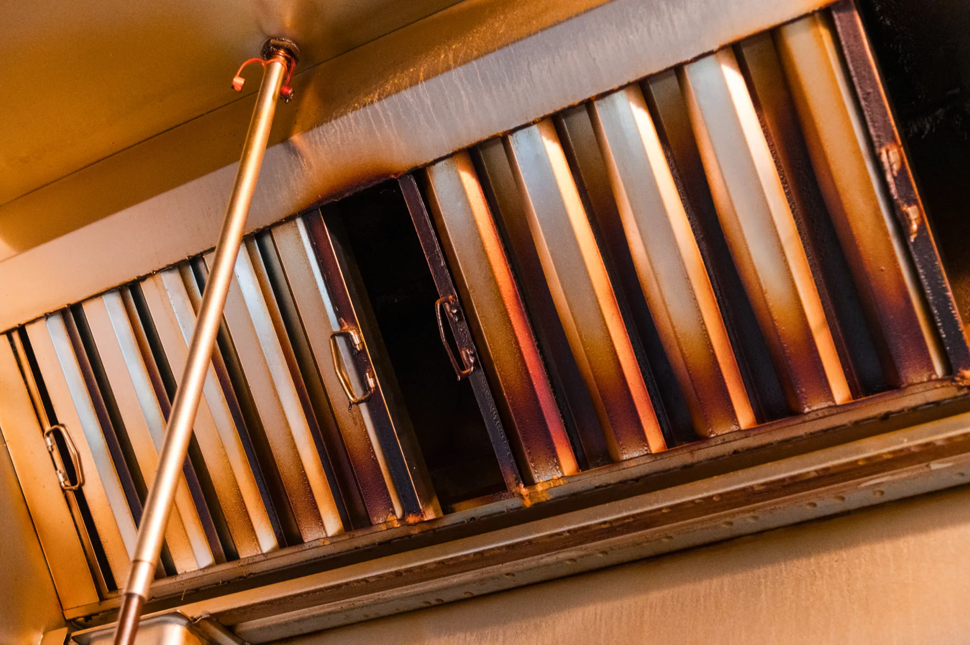 A close-up of a commercial kitchen hood filter being cleaned with a spray wand.