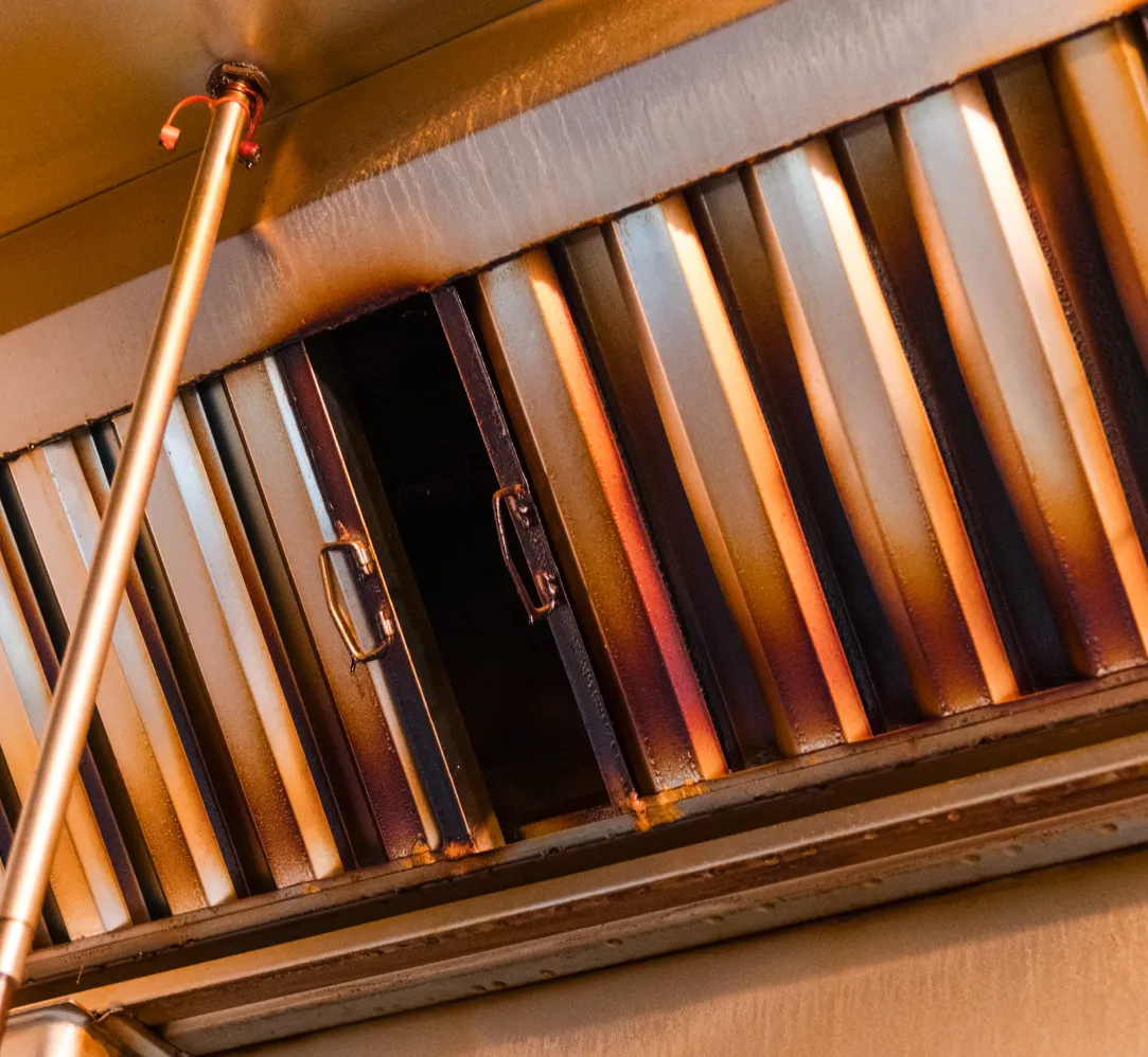 hood-2 Greasy metal kitchen exhaust hood with filters and pipes, showing signs of heavy use and discoloration.