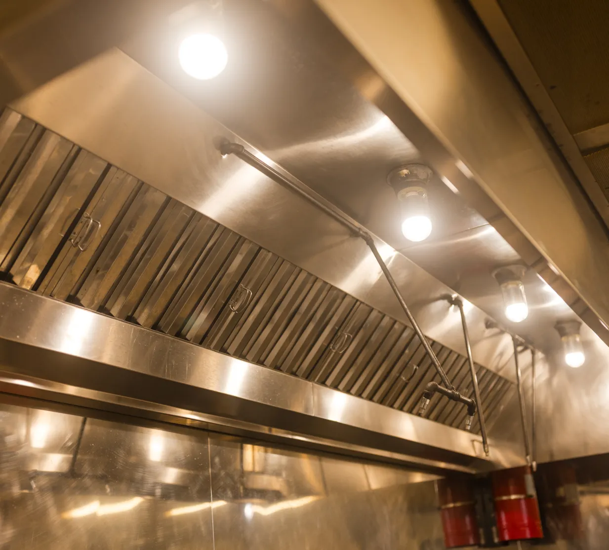 Stainless steel commercial kitchen hood with bright overhead lights and ventilation system.