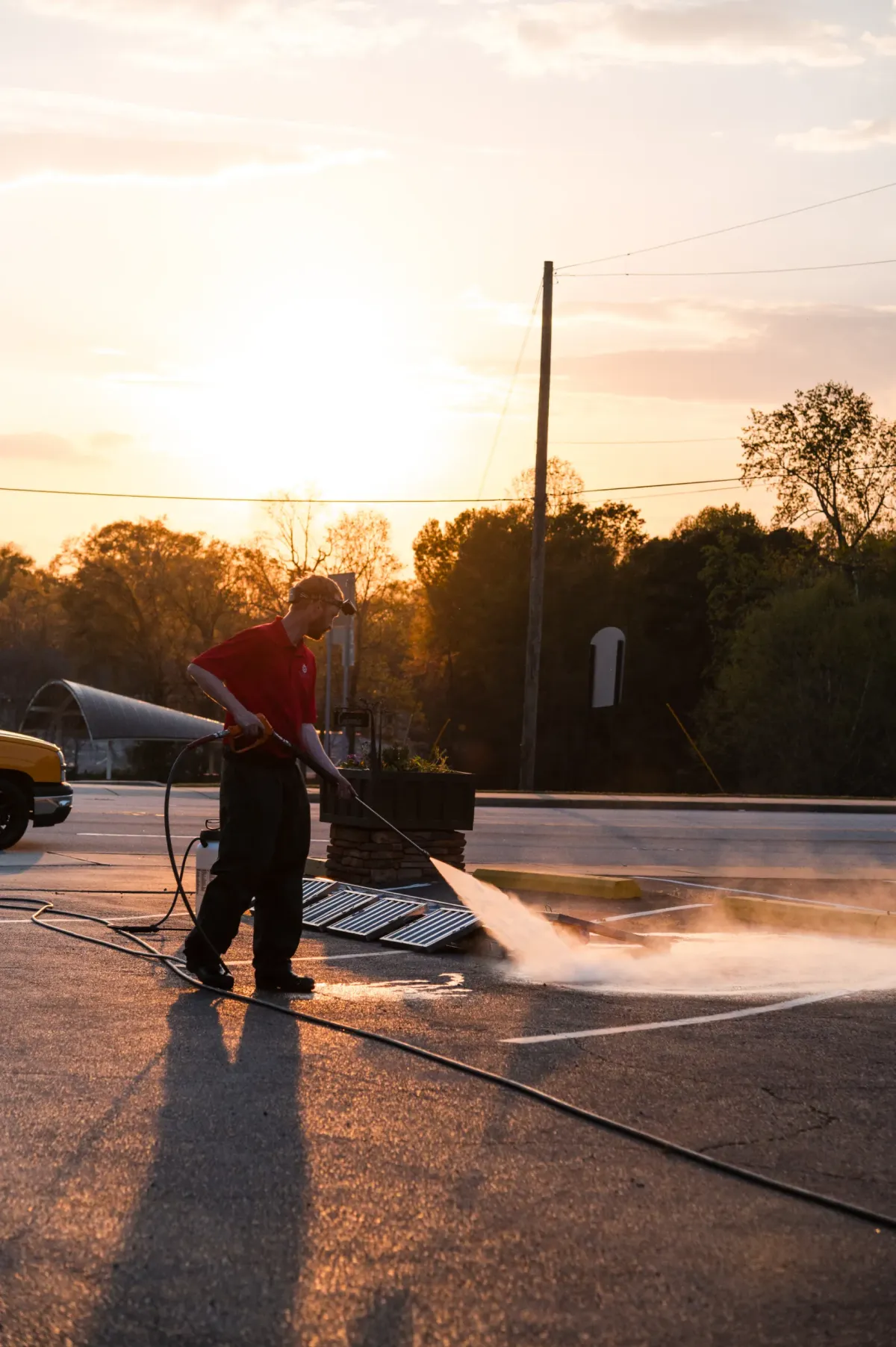 A person power washing a parking lot at sunset with water spraying from the hose.